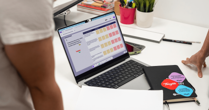 Vista di una scrivania con un portatile aperto che mostra il workshop Trasparenza by Design in FigJam, accanto a un taccuino Tangible con adesivi.