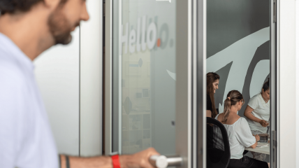 Una persona apre la porta d’ingresso di Tangible, mentre all’interno si intravedono alcune persone del team al lavoro negli spazi dell’ufficio.