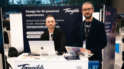 Stand Tangible ad AI Festival: team al desk il laptop davanti al pannello con scritto Design for AI-powered experiences.
