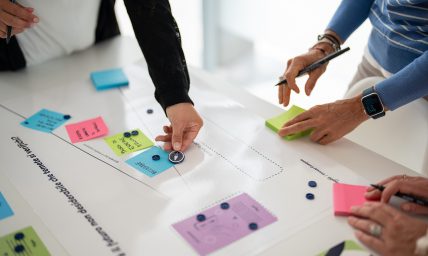 Mani che spostano post-it colorati e segnalini su una mappa di lavoro collaborativa.