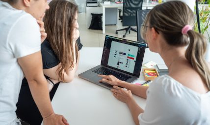 Three people around a laptop collaborating on a digital project.