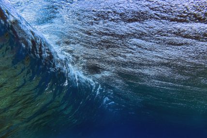 Vista subacquea di un’onda che si muove fluida e potente, con giochi di luce e riflessi blu che evocano profondità e movimento