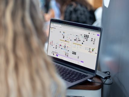 Laptop mostra una mappa di flussi e prototipi digitali su piattaforma di design collaborativo.
