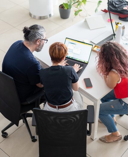 Tre persone attorno a un laptop collaborano su un progetto digitale.