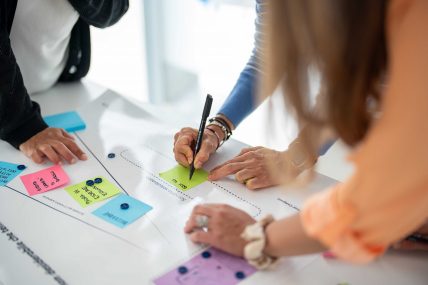 Tre persone lavorano insieme su un canva, utilizzando post-it colorati.