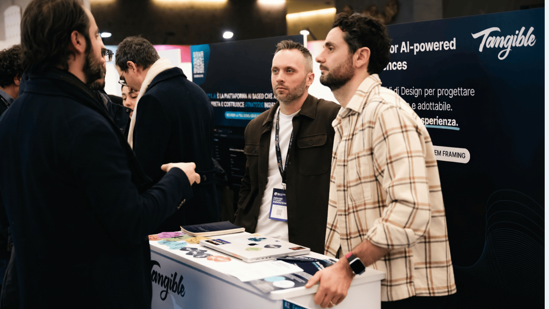 Persone che discutono davanti allo stand Tangible durante un evento, in un momento di confronto su temi di design e innovazione.